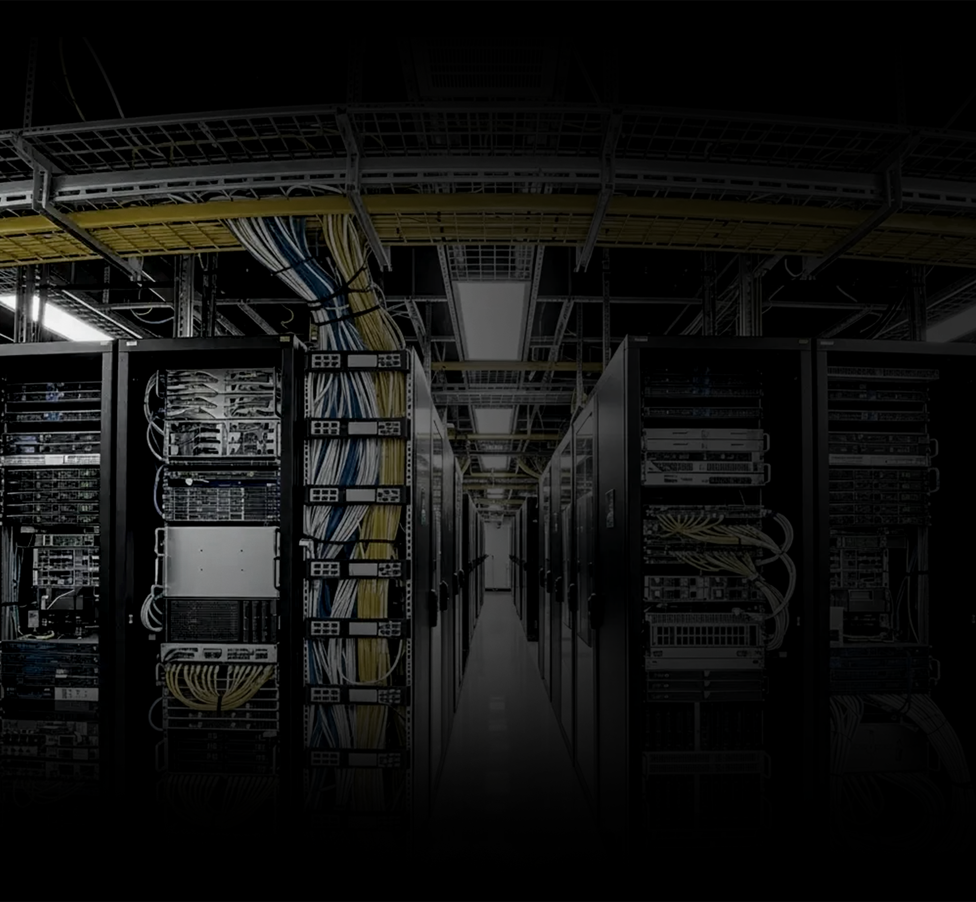 Server racks lining a data center aisle, with overhead cable trays and yellow and blue fiber runs